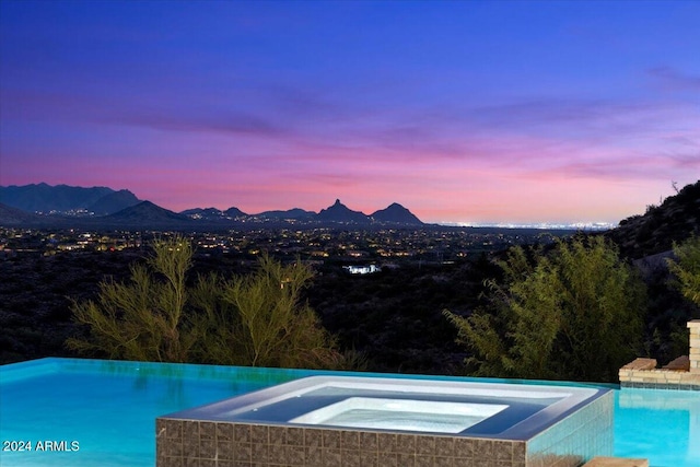 pool at dusk featuring a mountain view and an in ground hot tub