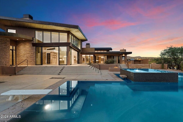 back house at dusk featuring a pool with hot tub and a patio