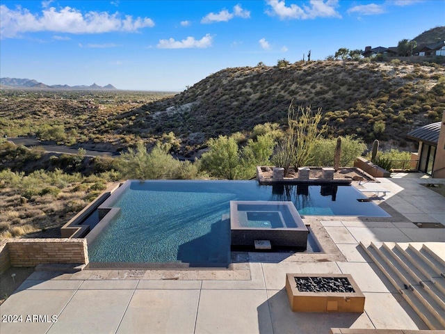 view of swimming pool featuring a mountain view, an in ground hot tub, a fire pit, and a patio area