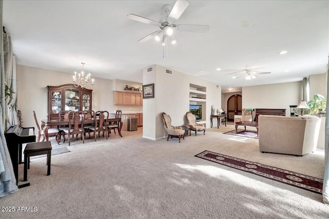 carpeted living room with ceiling fan with notable chandelier