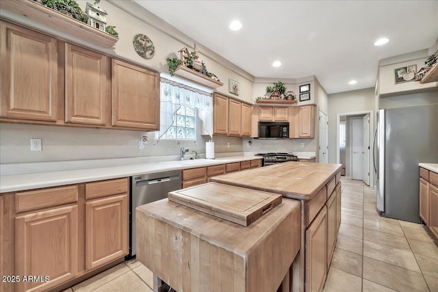 kitchen with light tile patterned floors, wooden counters, appliances with stainless steel finishes, a center island, and sink