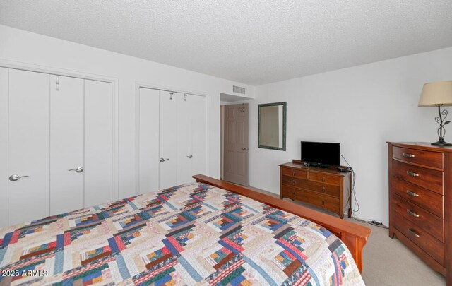 carpeted bedroom with a textured ceiling and two closets