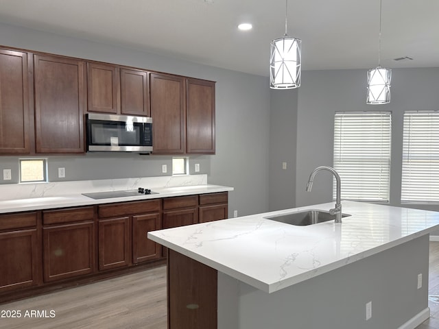 kitchen with stainless steel microwave, a sink, light wood-style floors, black electric stovetop, and decorative light fixtures