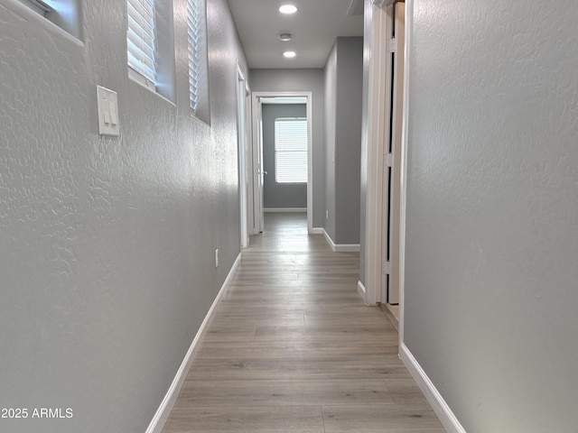 hall featuring baseboards, wood finished floors, and a textured wall