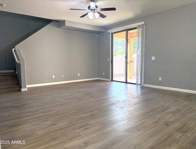 unfurnished living room with wood finished floors, a ceiling fan, stairs, and baseboards
