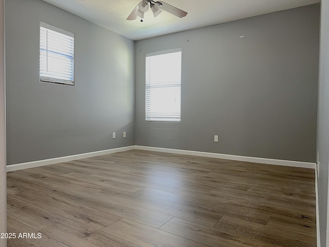 unfurnished room with a wealth of natural light, wood finished floors, a ceiling fan, and baseboards