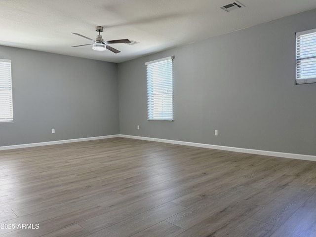 empty room with a ceiling fan, visible vents, wood finished floors, and baseboards