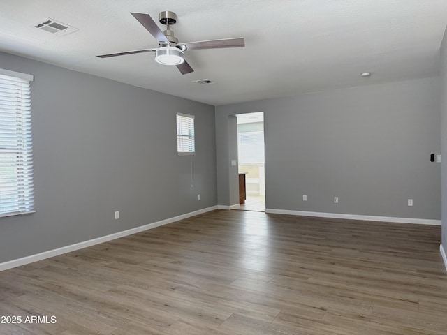 empty room featuring wood finished floors, visible vents, ceiling fan, and baseboards