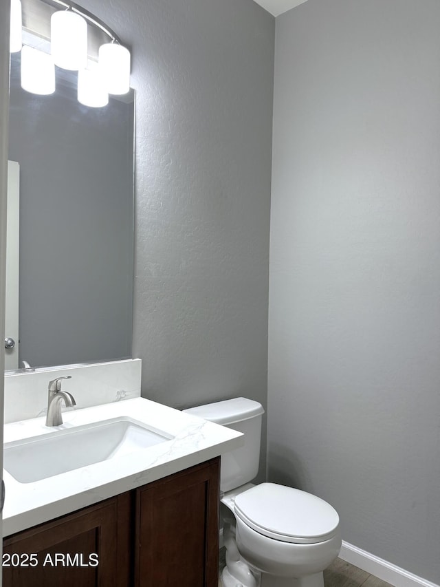 half bathroom with baseboards, toilet, a textured wall, and vanity