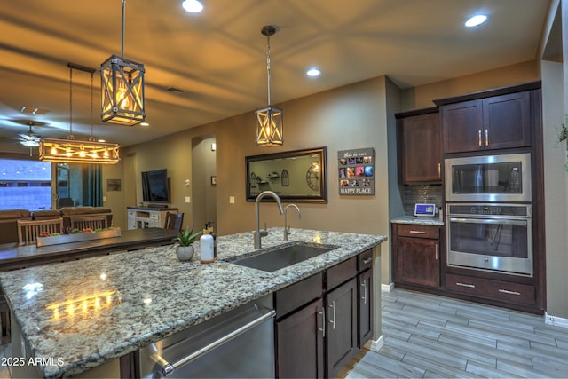 kitchen featuring decorative light fixtures, stainless steel appliances, a kitchen island with sink, ceiling fan, and sink