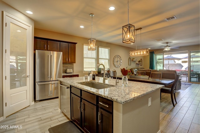 kitchen featuring a kitchen island with sink, appliances with stainless steel finishes, pendant lighting, dark brown cabinetry, and sink