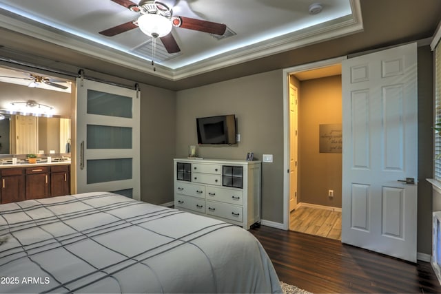 bedroom featuring ceiling fan, ensuite bath, a barn door, and a tray ceiling