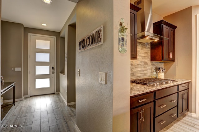 kitchen featuring light hardwood / wood-style floors, stainless steel gas cooktop, light stone counters, decorative backsplash, and wall chimney range hood