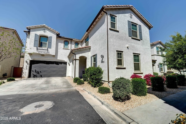 mediterranean / spanish house featuring an attached garage, a tiled roof, concrete driveway, and stucco siding