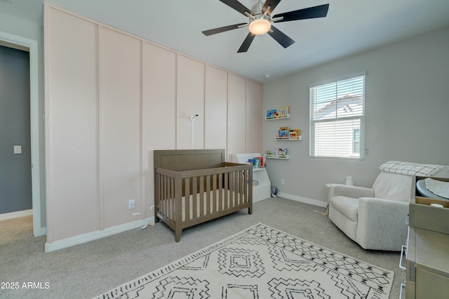 bedroom with baseboards, ceiling fan, a crib, and light carpet