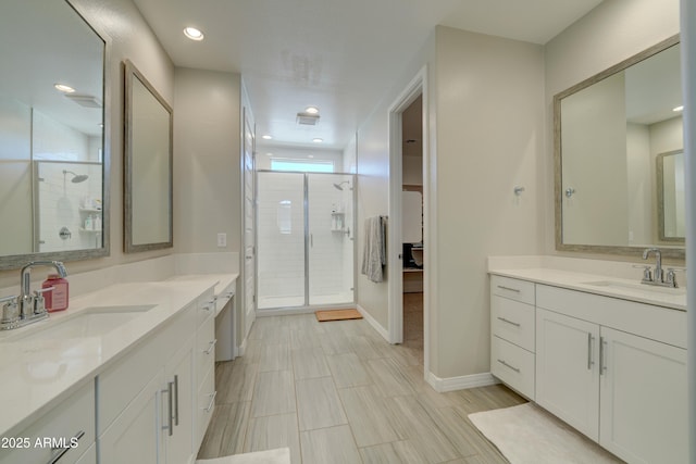 full bath with a sink, two vanities, a stall shower, and baseboards