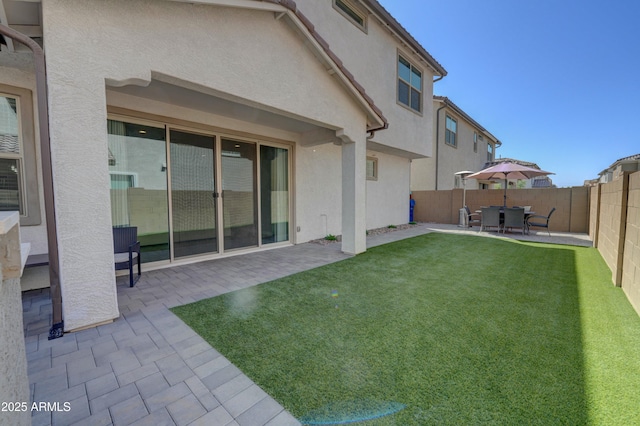 rear view of house featuring a patio, stucco siding, a fenced backyard, and a lawn