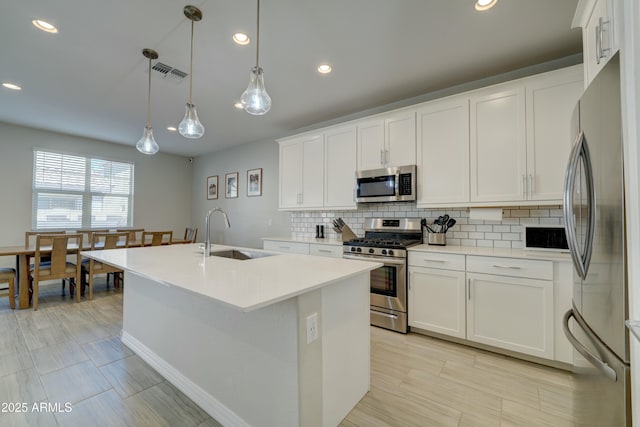 kitchen with white cabinets, visible vents, appliances with stainless steel finishes, a sink, and backsplash
