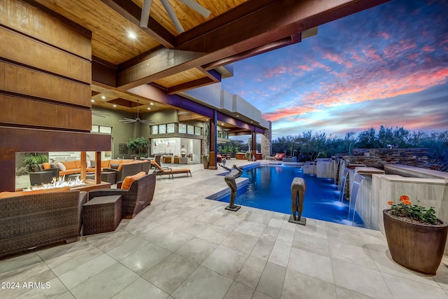 pool at dusk with pool water feature, an outdoor living space with a fire pit, ceiling fan, and a patio area