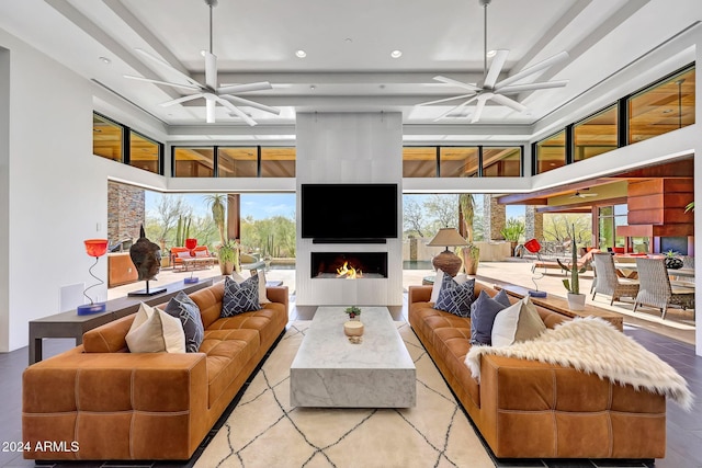 living room featuring a towering ceiling, ceiling fan, a fireplace, and a wealth of natural light