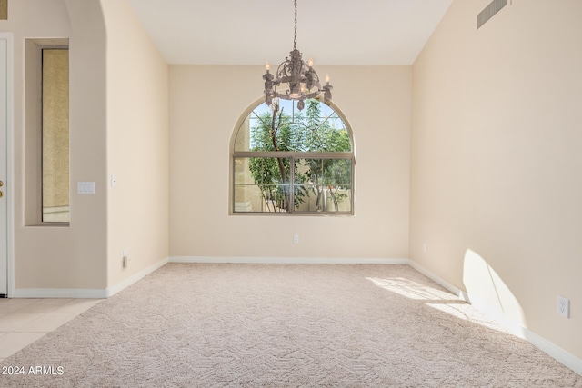 spare room featuring a chandelier and light carpet