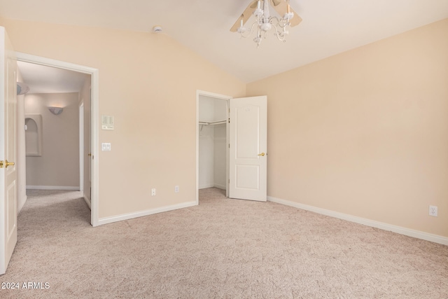 unfurnished bedroom featuring a closet, lofted ceiling, a walk in closet, and light colored carpet