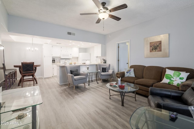 living area with visible vents, a textured ceiling, light wood finished floors, and ceiling fan with notable chandelier