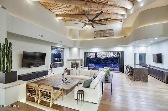 living room featuring beam ceiling, light wood finished floors, visible vents, wooden ceiling, and a lit fireplace