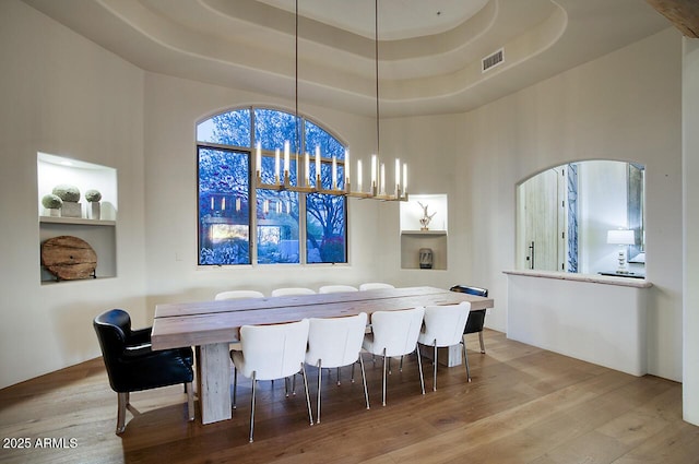 dining area with a high ceiling, wood finished floors, visible vents, a raised ceiling, and an inviting chandelier