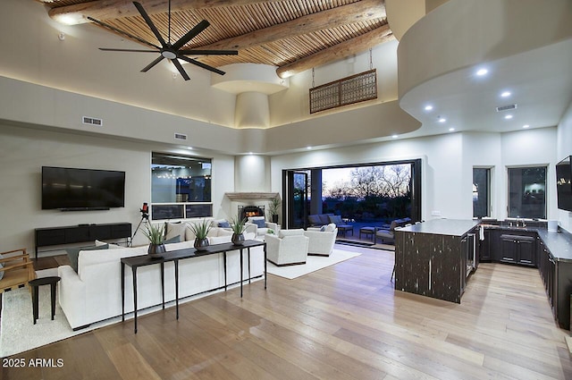 living room with visible vents, wood ceiling, beamed ceiling, a lit fireplace, and light wood-type flooring