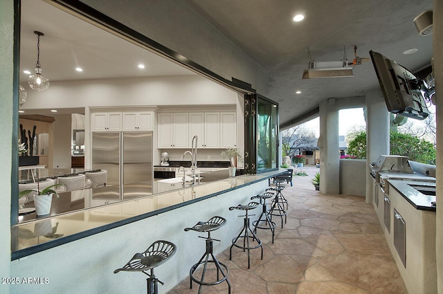 kitchen with stone tile floors, a breakfast bar, a sink, white cabinetry, and stainless steel built in refrigerator