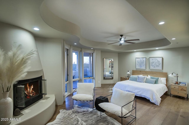 bedroom with recessed lighting, a raised ceiling, a fireplace, and wood finished floors