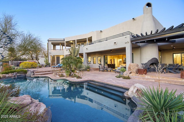 back of house featuring a balcony, a patio area, an outdoor pool, and an outdoor living space