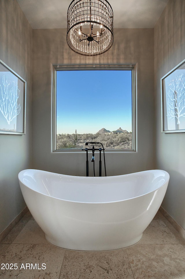 bathroom with speckled floor, an inviting chandelier, a freestanding tub, and baseboards