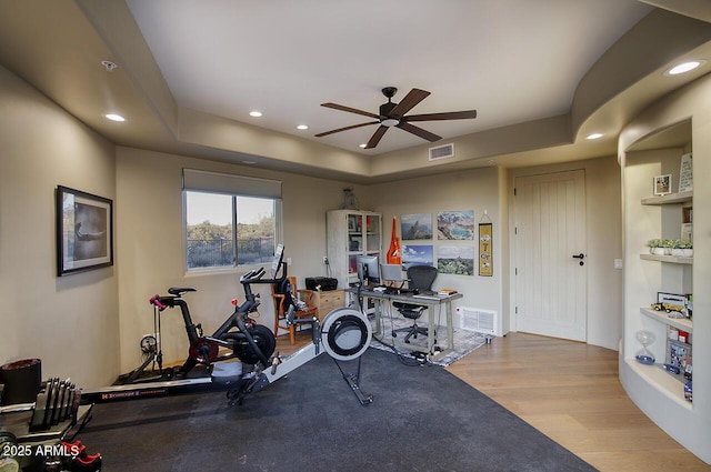 exercise room featuring a raised ceiling, wood finished floors, visible vents, and recessed lighting