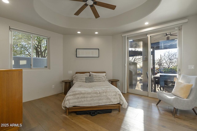 bedroom with a tray ceiling, recessed lighting, wood finished floors, and access to exterior