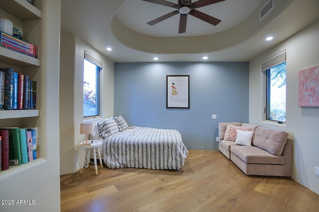 bedroom featuring a tray ceiling, wood finished floors, visible vents, and recessed lighting