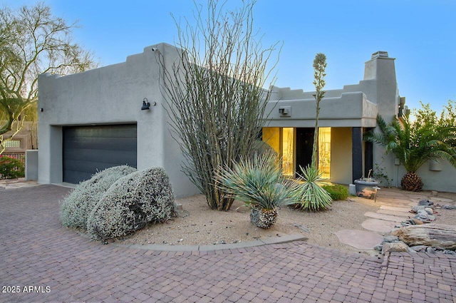 view of front of home with decorative driveway, an attached garage, and stucco siding