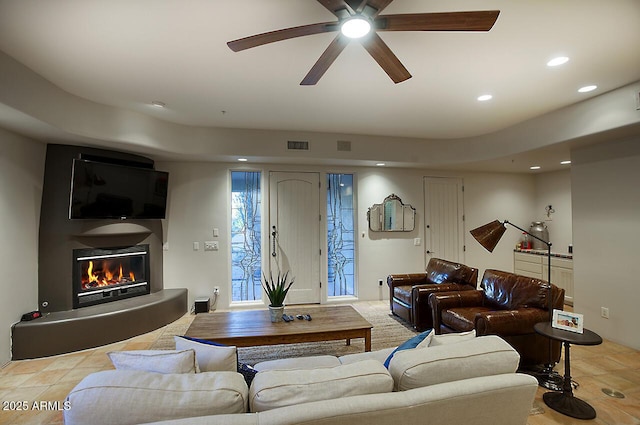 living room with a ceiling fan, a glass covered fireplace, visible vents, and recessed lighting