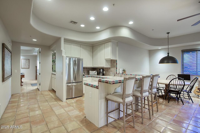 kitchen with tasteful backsplash, visible vents, freestanding refrigerator, a peninsula, and a kitchen bar