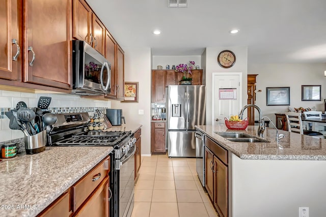 kitchen featuring decorative backsplash, light tile patterned floors, appliances with stainless steel finishes, a sink, and a center island with sink