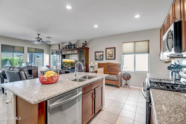 kitchen with a kitchen island with sink, a sink, light tile patterned floors, appliances with stainless steel finishes, and open floor plan