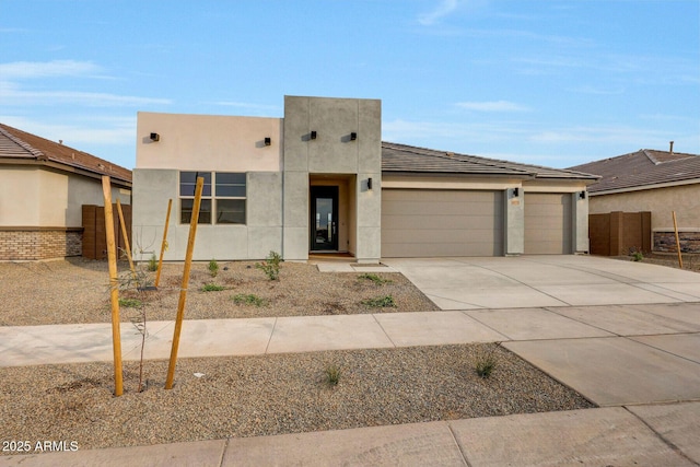 pueblo revival-style home with stucco siding, an attached garage, driveway, and fence