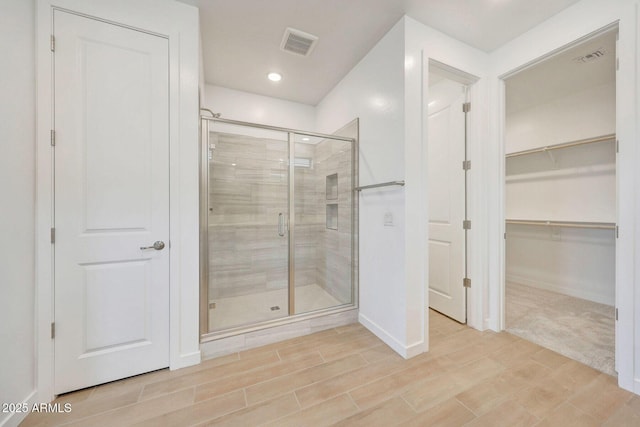 bathroom with visible vents, a walk in closet, a stall shower, baseboards, and wood tiled floor