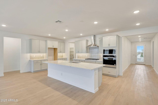 kitchen with light wood finished floors, stainless steel gas cooktop, built in microwave, a sink, and wall chimney exhaust hood