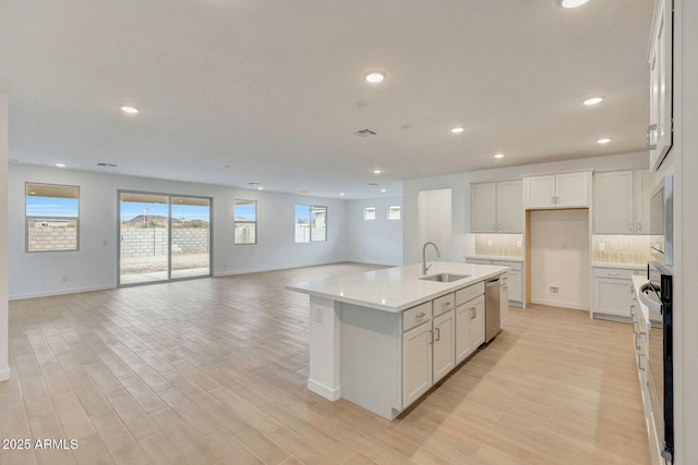 kitchen with light wood finished floors, a sink, dishwasher, open floor plan, and backsplash