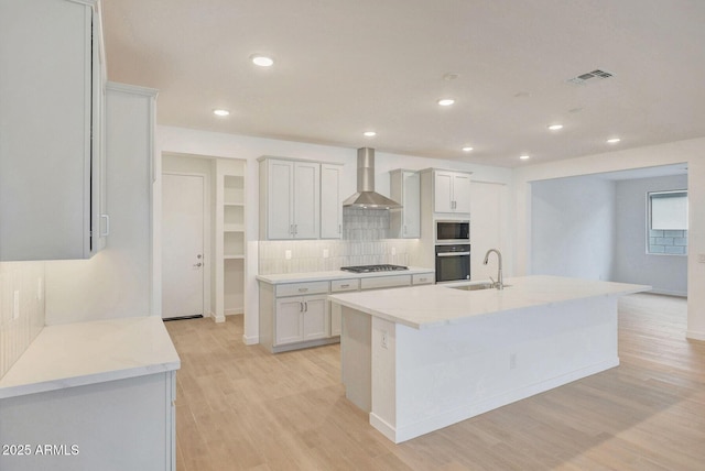 kitchen featuring visible vents, light wood finished floors, appliances with stainless steel finishes, wall chimney range hood, and tasteful backsplash