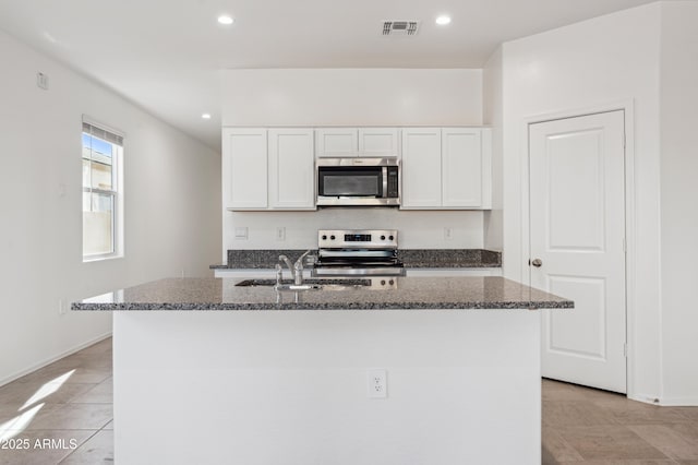 kitchen with stainless steel appliances, visible vents, an island with sink, and dark stone counters