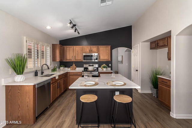 kitchen with arched walkways, stainless steel appliances, light countertops, a sink, and lofted ceiling