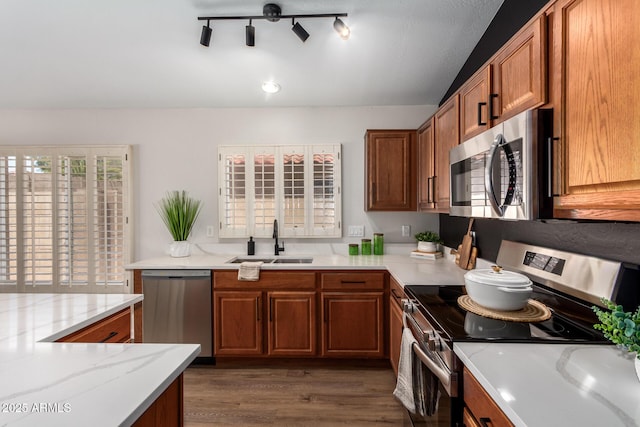 kitchen with light stone countertops, brown cabinets, a sink, appliances with stainless steel finishes, and wood finished floors